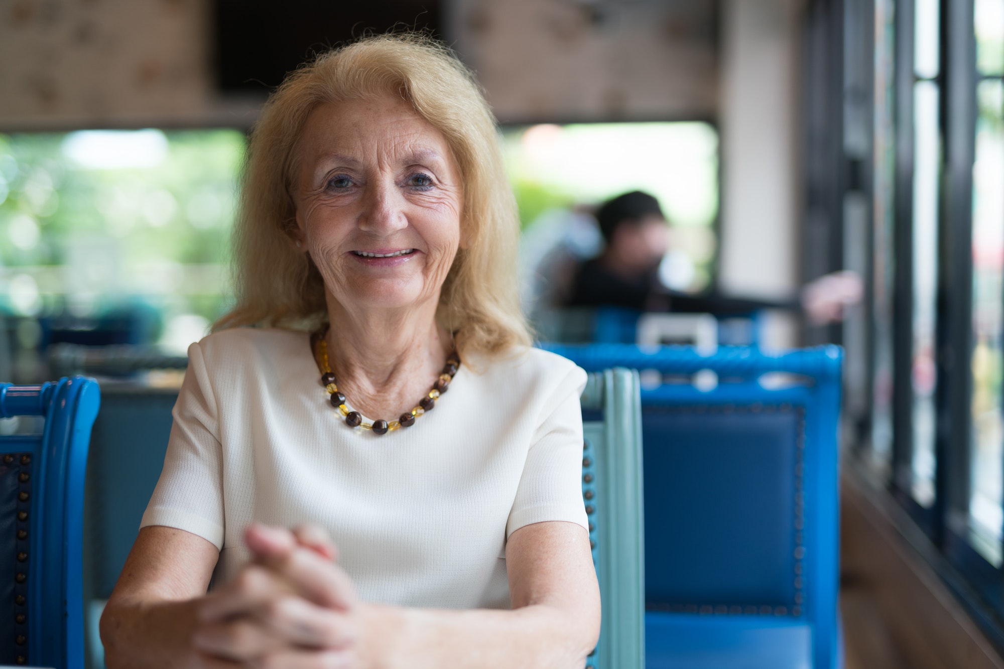 Portrait of happy senior woman smiling and looking at camera while sitting at restaurant
